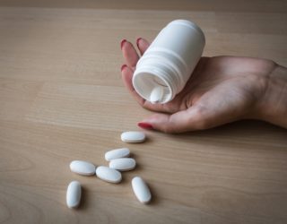 Lunesta Withdrawal Symbolized by a Hand Holding a Pill Bottle with Pills Spilling onto a Wood Floor
