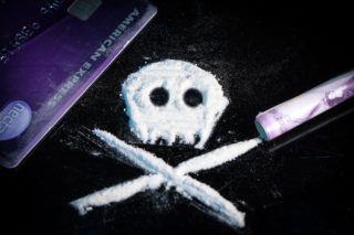 credit card, rolled bill and white powder in form of a skull on a black table