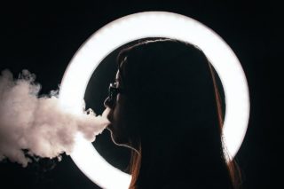 woman standing beside round lightbulb while smoking