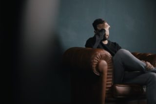 man sitting in couch grabbing his head with one hand
