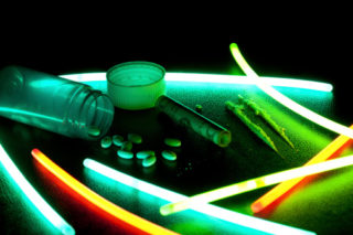 Prescription drugs laid out next to glow sticks with a rolled up twenty dollar bill.