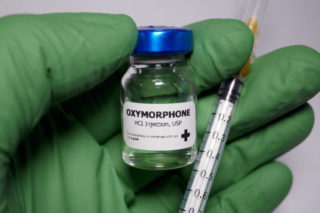 Hand with green glove holding a Oxymorphone flask and a syringe
