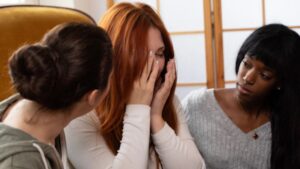Young woman is crying while two friends comfort her