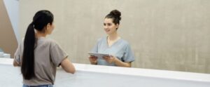 A smiling receptionist with a tablet assists a patient at a medical facility